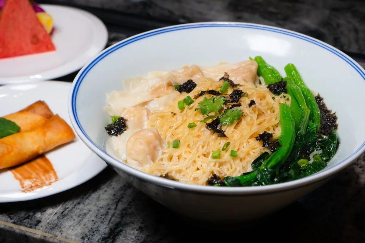A bowl of noodles topped with wontons and greens
