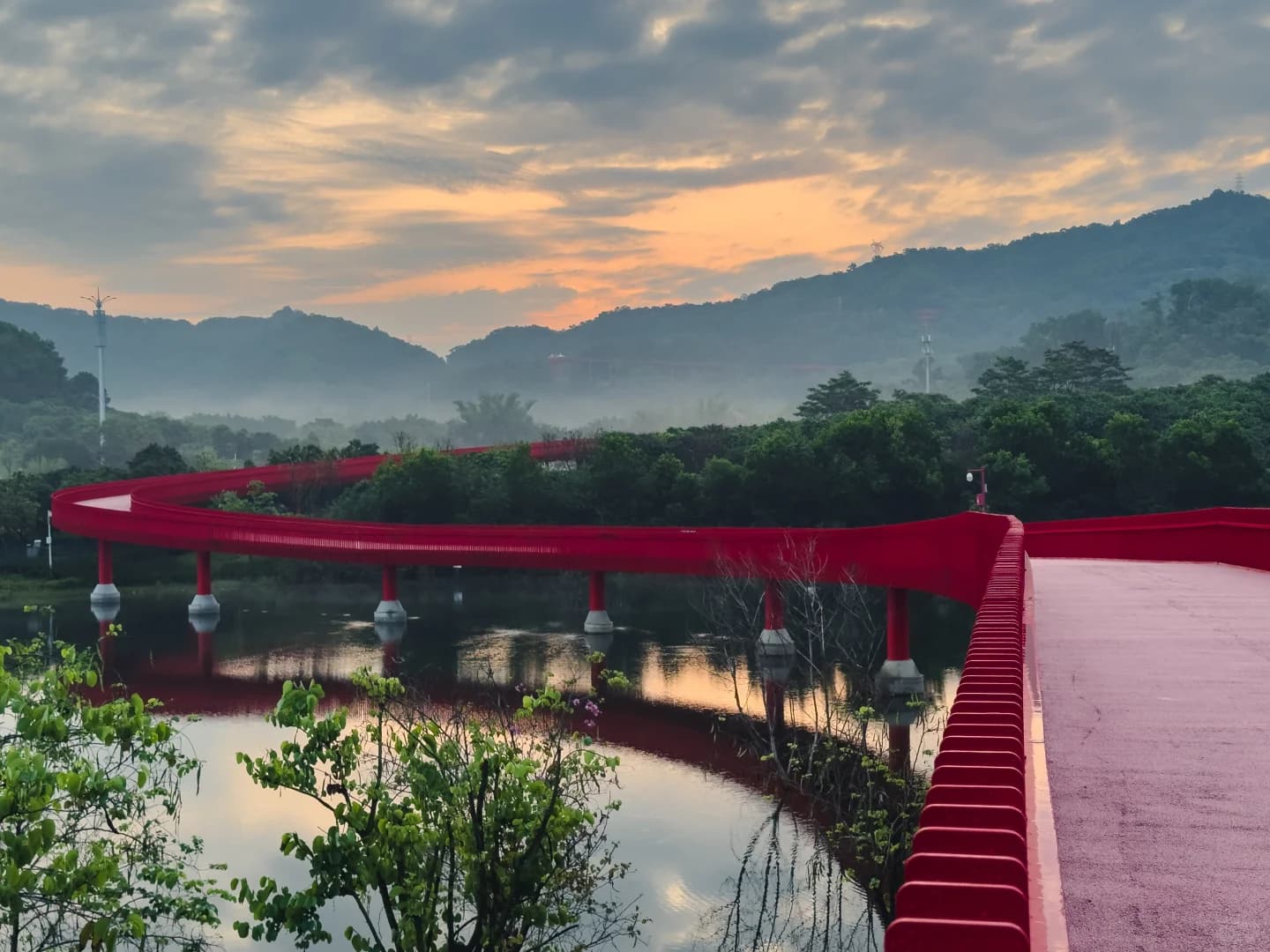Hongqiao Park's red walkway crossing the lake beneath hills at sunrise