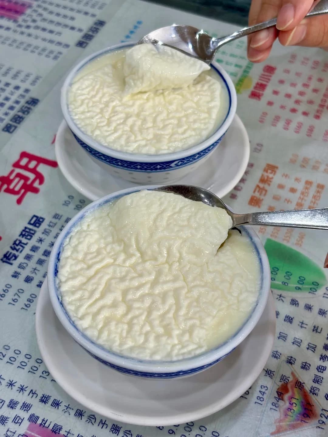 Two bowls of double-skin milk with the surface and spoonfuls visible
