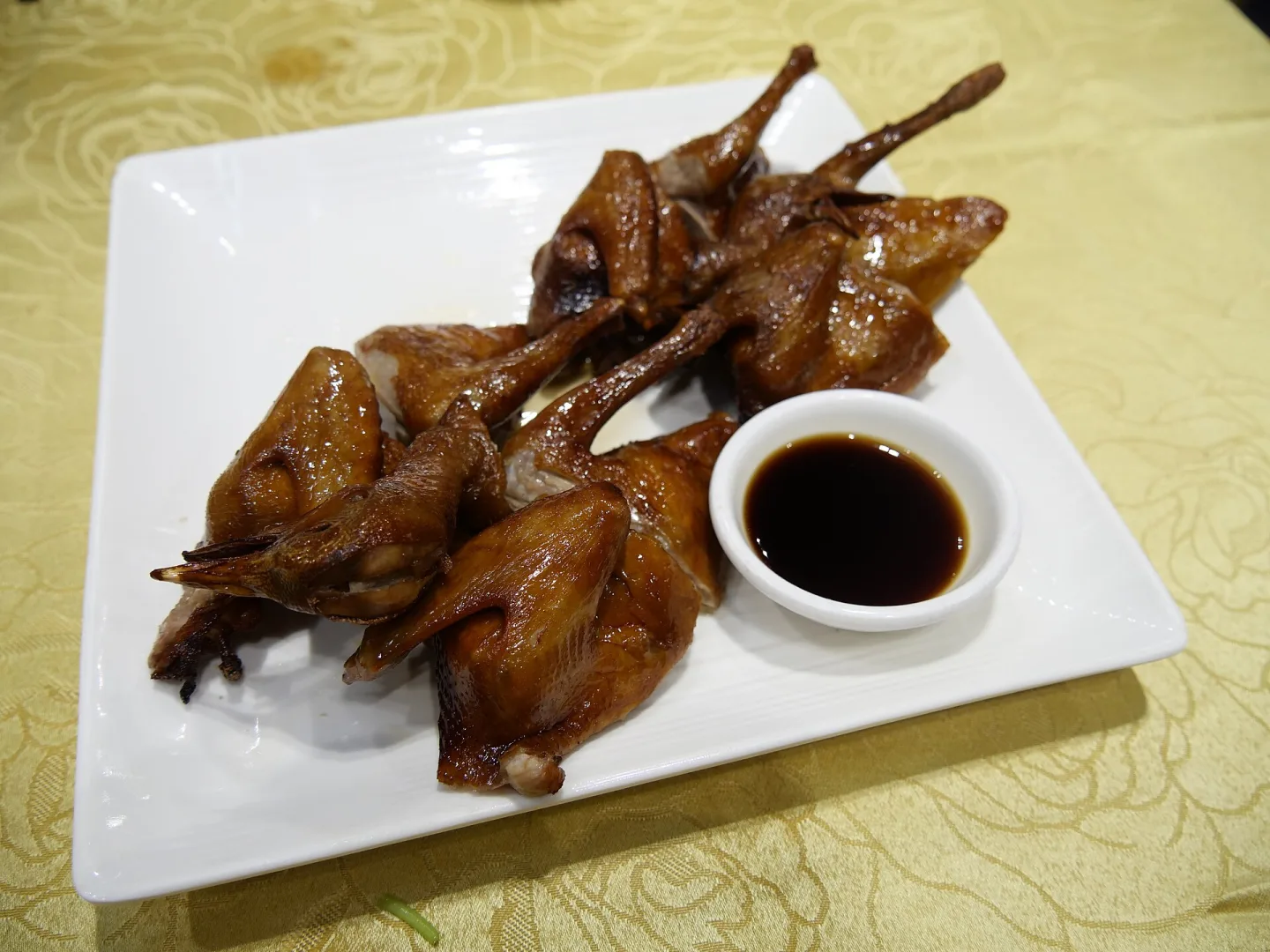 Whole baked pigeons served on a white plate with sauce